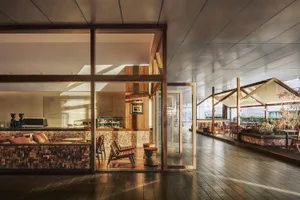 A modern restaurant interior with a wooden floor, dining tables, and chairs, featuring a large window and soft warm lighting