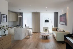 A modern living room with a white couch, chair, and dining table, featuring wood and glass materials, natural light, and a clean design