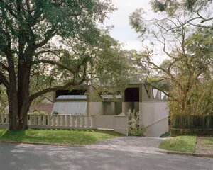 A modern house with a white exterior, surrounded by trees, featuring a large window and a calm, serene atmosphere