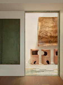 A modern room with a green wall and white floor, featuring a doorway, window, and three small stools, with dim lighting creating a cozy atmosphere