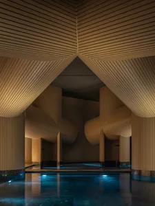 A large indoor pool area with a wooden ceiling and pillars surrounding the pool, creating a calm and inviting atmosphere