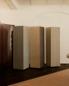 A minimalist living space with three tall wooden pillars, a bench in the corner, and a clean design aesthetic