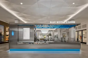 A modern coffee shop with a blue and white color scheme, featuring a variety of seating options, potted plants, and a welcoming atmosphere