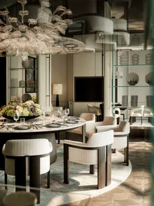 A well-lit dining room with a round table, chairs, vases, and a chandelier, surrounded by wood and glass surfaces