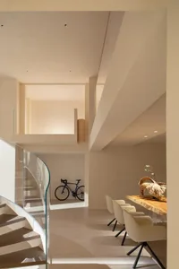 Modern living room with a glass staircase, dining table, and wooden furniture, well-lit with natural light
