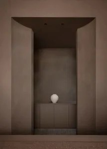 A small, simple room with a brown color scheme and a white vase on a counter as the main point of interest