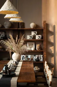 Dining room with a wooden table, chairs, and bookshelf, set with various items and decorated with vases, surrounded by natural light