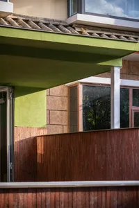 A modern house with a green roof, wooden fence, and large window, set against a bright and warm background