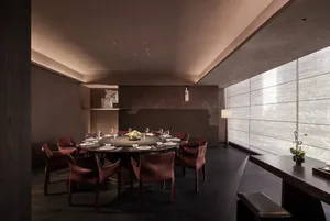 Elegant dining room with a round table, brown chairs, and a large window allowing natural light