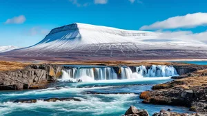 A serene mountain landscape with a waterfall flowing down its rocky side, set against a blue sky with natural sunlight