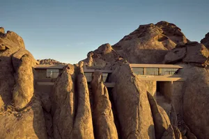 A serene mountain retreat with a stone house and a mountain visible through the windows, bathed in natural light