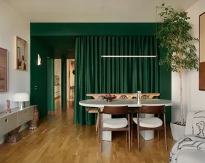 Dimly lit dining room with a green table and chairs, surrounded by a potted plant, in a modern style with a focus on comfort and functionality