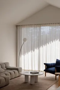 Cozy living room with a white couch, chair, and dining table, decorated with white curtains and a lamp, creating a warm and inviting atmosphere