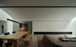 A well-lit living room and kitchen with a couch, chair, coffee table, dining table, counter, and decorative items, featuring wood and glass materials