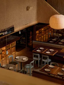 Cozy restaurant interior with wooden floor, dining tables, chairs, and wine bottles, dim lighting creates an intimate ambiance