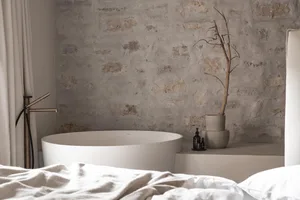 Cozy minimalist bedroom with a white bed and stone wall, featuring a bathtub and soft diffused lighting