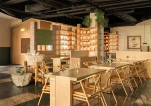 A modern restaurant interior with multiple tables, chairs, and potted plants, well-lit and welcoming