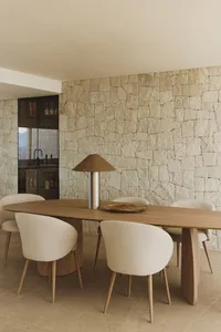 A modern dining room with a wooden table and chairs surrounded by a stone wall, well-lit for a warm and inviting atmosphere