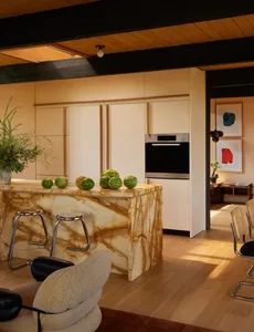 Modern kitchen with a marble countertop, featuring a refrigerator, oven, and sink, with natural light and comfortable seating