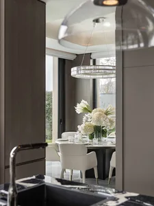 Dining room with a large window, a chandelier, and a table with white chairs, set with a vase of flowers, in a modern space with natural light