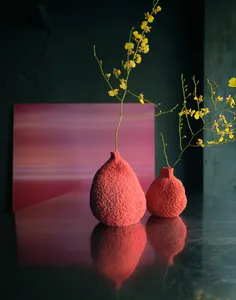 A dimly lit room with a pink wall and two red vases on a table, the main focus of the scene