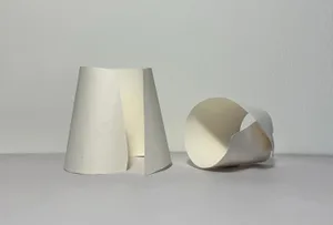 A minimalist room with three white objects stacked on a table against a white wall