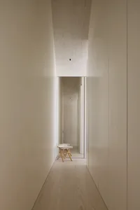 Narrow hallway with a white color scheme, a small table, and a chair, creating a cozy atmosphere with dim lighting