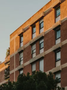 Photograph of a modern building with a brick facade, featuring a mix of brown and white colors, and numerous glass windows