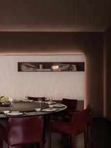 Dining room with a round table set with wine glasses and a vase, surrounded by chairs in a brown color scheme, with dim lighting creating a cozy atmosphere