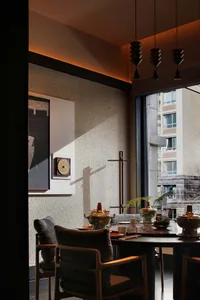 Dining room with a wooden table, chairs, and a window, set with various dishes and a potted plant, with natural light from the window creating a warm and inviting atmosphere