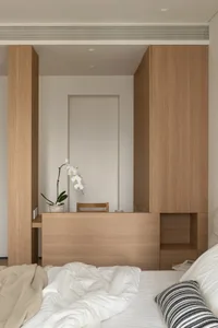 A cozy bedroom with a wooden floor, white walls, a bed, a desk, and a chair, creating a comfortable atmosphere