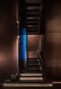 A dimly lit staircase with a metal railing and a blue wall in a mysterious atmosphere