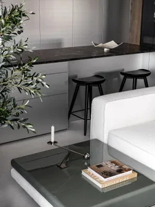 Modern living room with a white couch, glass coffee table, marble countertop, and black and white theme, featuring three black stools and a potted plant