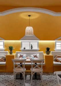 A cozy restaurant with a yellow color scheme, featuring a table with white chairs and potted plants, creating a warm and inviting atmosphere