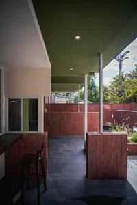 A modern dining-living space with a red brick wall, green roof, dining table, chairs, and natural light from a large window