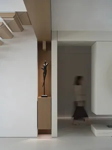 A woman in a brown coat walks down a calm and quiet hallway with wooden walls and floor
