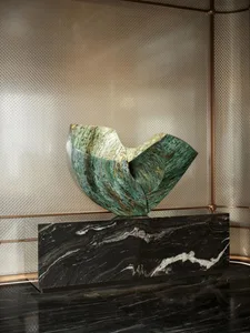 A modern art sculpture displayed on a stone pedestal in a room with a metallic wall and a silver-like color scheme