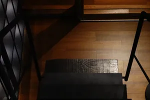 A dimly lit, vintage staircase with dark wooden treads and a wooden floor, set against a neutral background