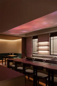 a modern restaurant interior with a long wooden table, chairs, wine glasses, and a potted plant, soft warm lighting