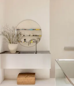 A well-lit bathroom with a sink, mirror, and vase, featuring predominantly white materials