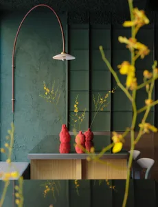 A modern dining room with a green wall, a dining table, and chairs, featuring a red vase and natural lighting