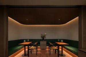 A modern dining space with a wooden floor and green benches, surrounded by chairs and wine glasses, creating a warm and inviting atmosphere