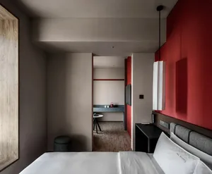 A warm and inviting hotel bedroom with a red-painted room, a black and white color scheme, and a bed positioned against a red wall, accompanied by a table and chair