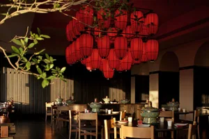 A modern dining space with a wooden floor, a dining table, and chairs, set with various bowls and cups, in a warm and welcoming atmosphere