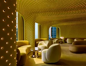 A large, open room with a yellow color scheme, featuring multiple seating areas, dining tables, and a welcoming atmosphere