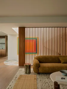 A modern living room with a yellow couch, a chair, and a dining table, featuring wooden elements, a rug, and natural light from the windows