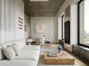 A modern living room with a large couch, dining table, and TV, featuring white walls and a neutral color palette, with soft and diffused lighting creating a cozy atmosphere