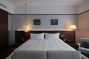 A well-lit bedroom with a large bed, wooden headboard, and nightstand, featuring a lamp and a picture above the bed