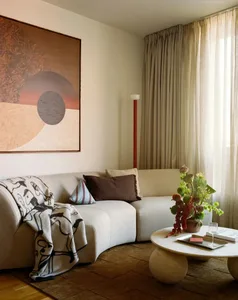 Cozy living room with a white couch, a red lamp, and natural light from the window, decorated with a vase and a potted plant