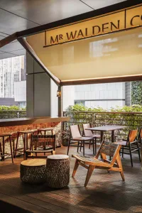 A dimly lit restaurant with a wooden floor, chairs, dining tables, and a bar, featuring a mix of wood and metal elements